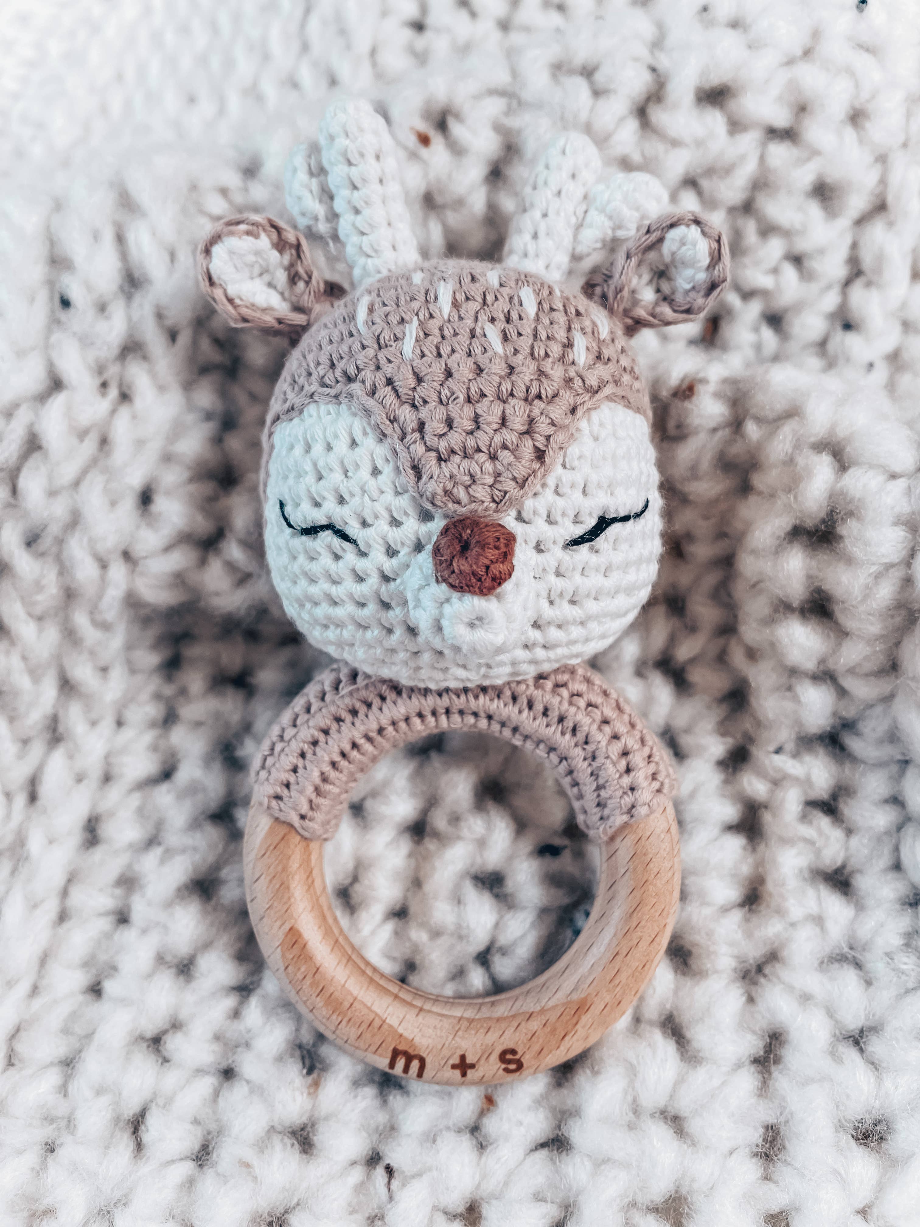 Handmade crochet deer rattle by Marlowe and Sage on cozy blanket, perfect sensory toy for babies, eco-friendly and soothing.