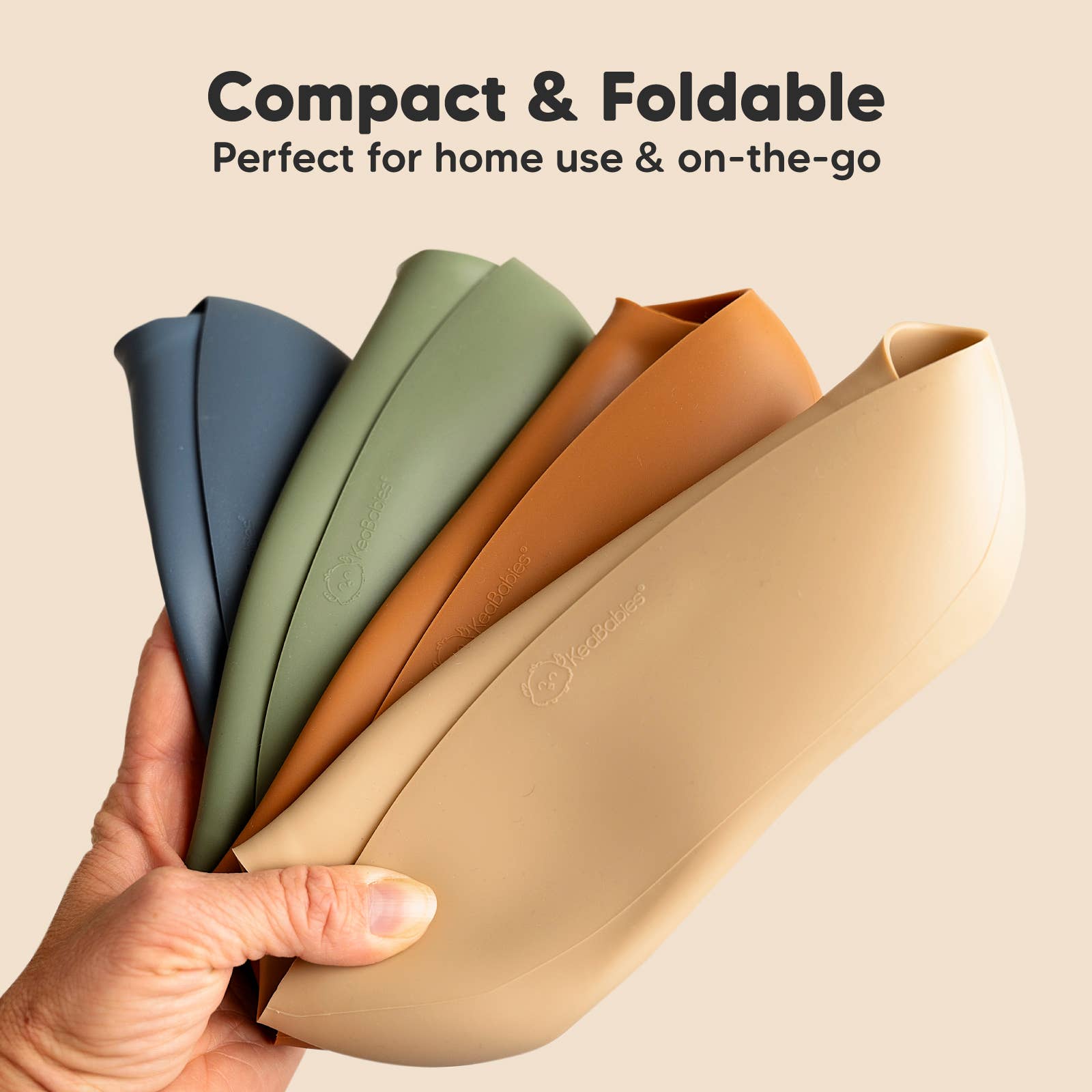 Hand holding four compact and foldable silicone bibs, perfect for home use and on-the-go feeding.