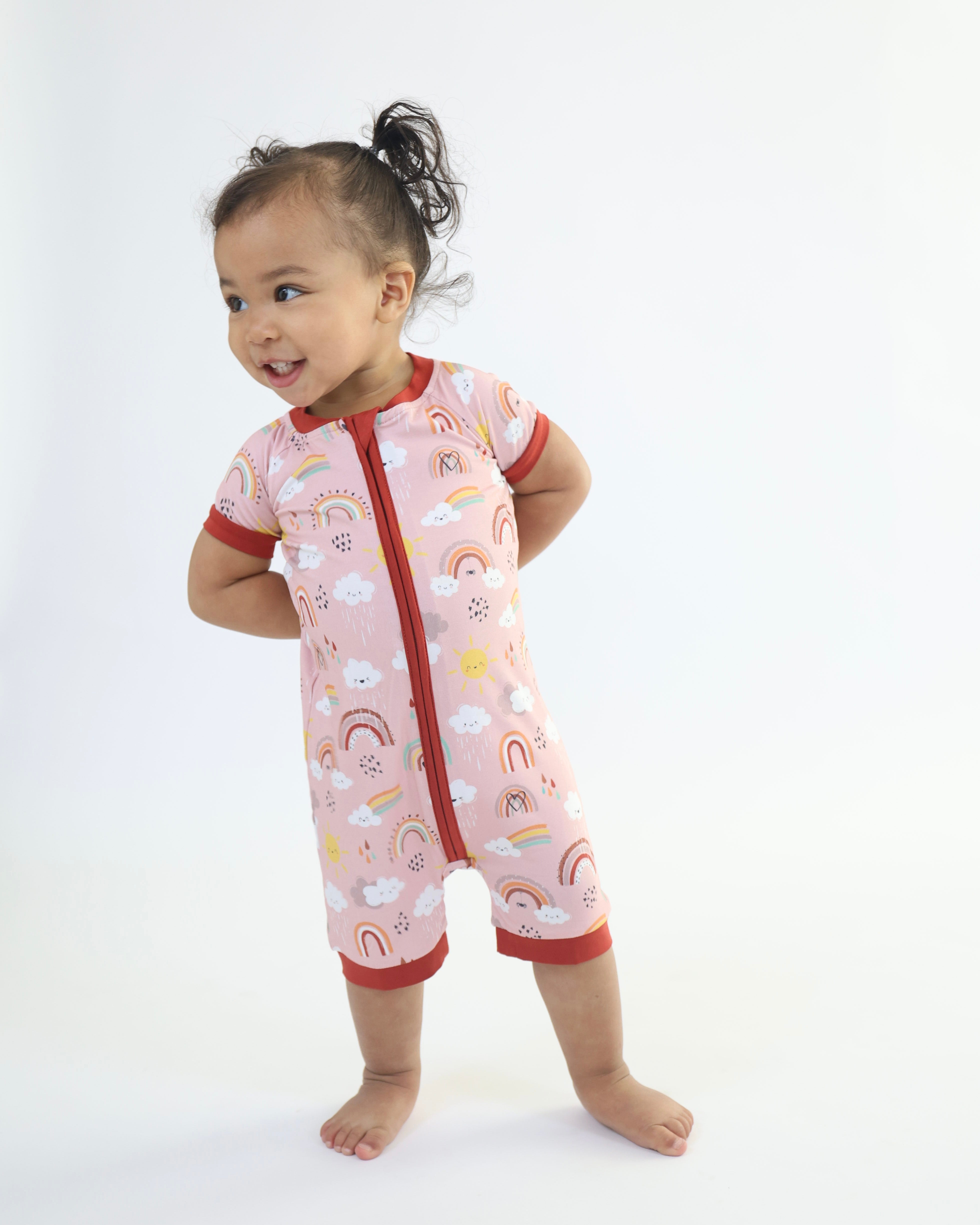 Toddler wearing Rainnbow Short Zipp Romper, vibrant patterns of rainbows and clouds, perfect for playtime.