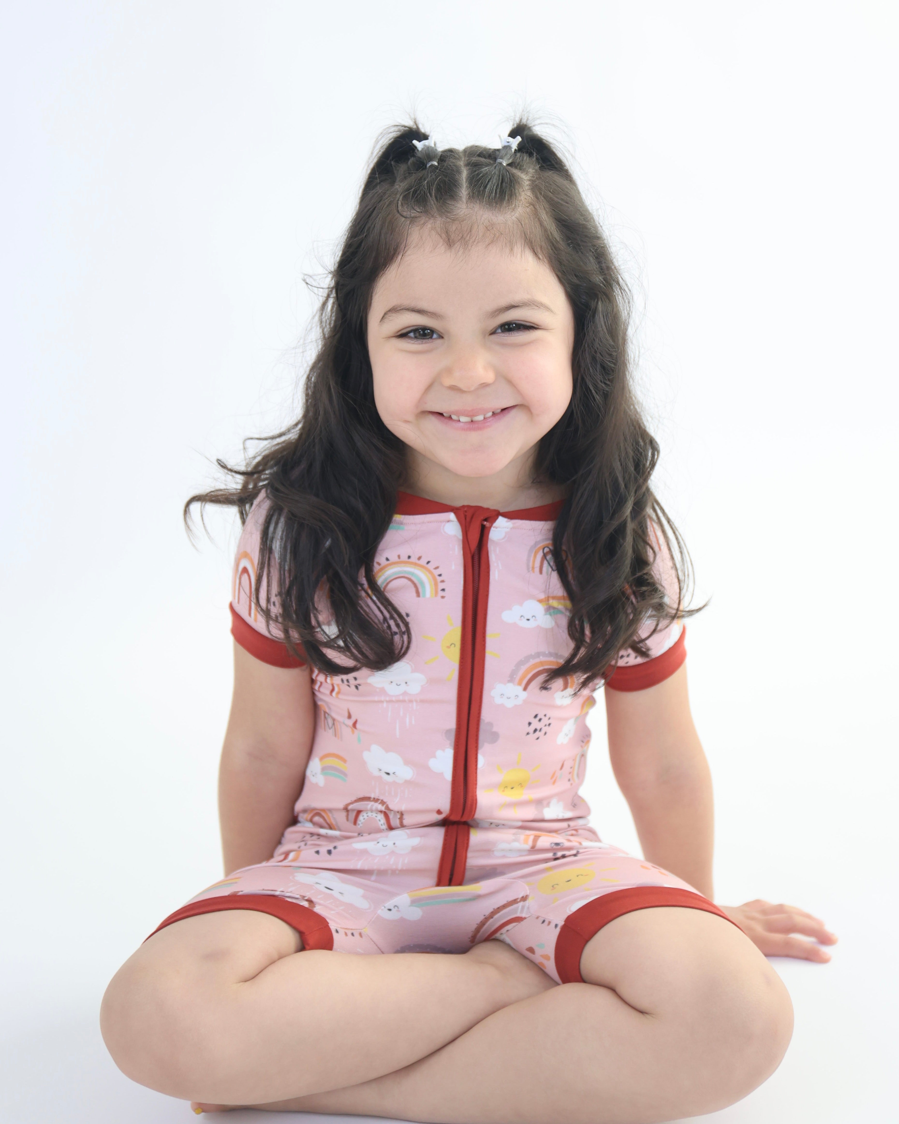 Child wearing Bamboo Short Romper with rainbow patterns by Rainn, showcasing soft and breathable fabric sitting on the floor.