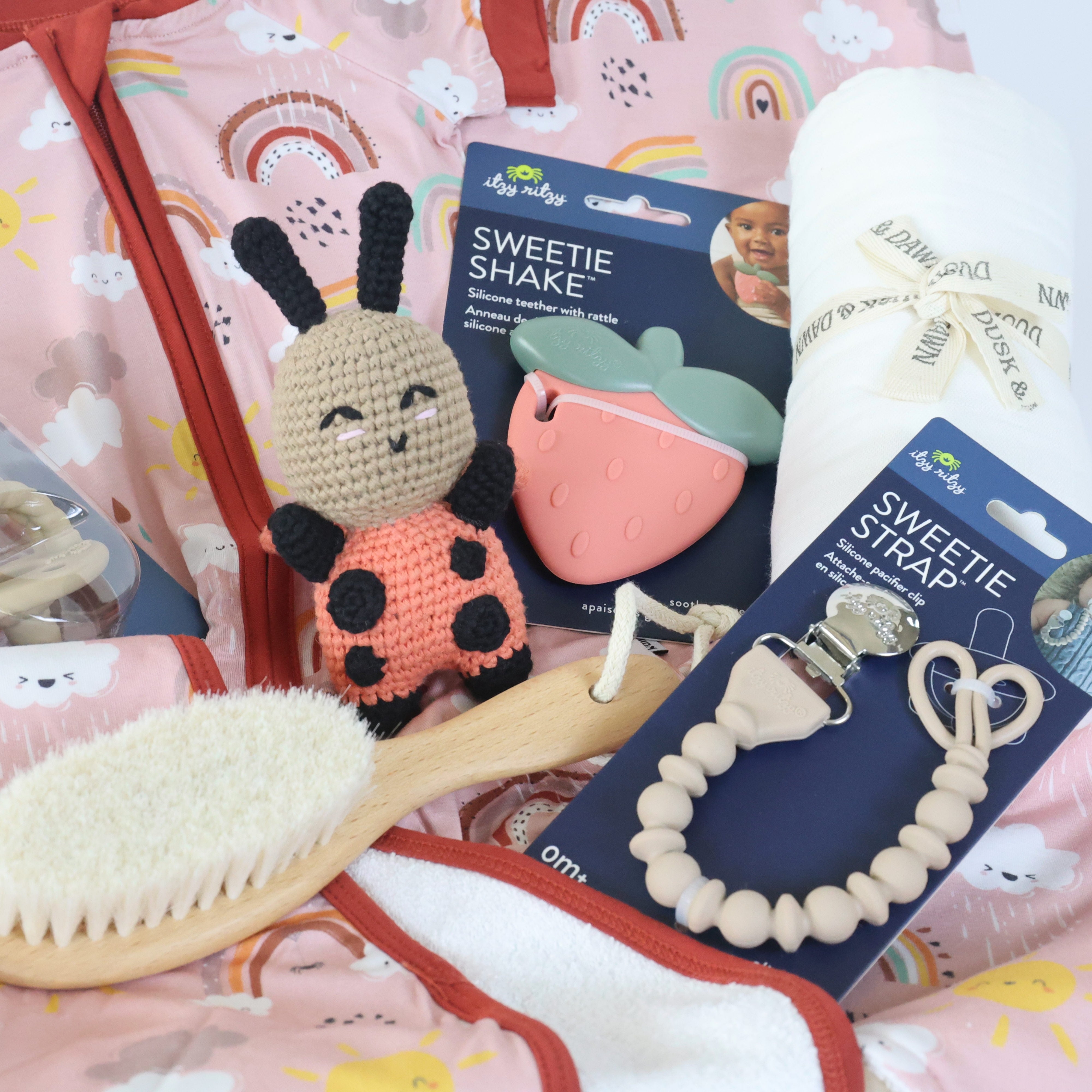 Newborn gift set for girls featuring soft toys, teether, brush, and a blanket in a colorful bag.