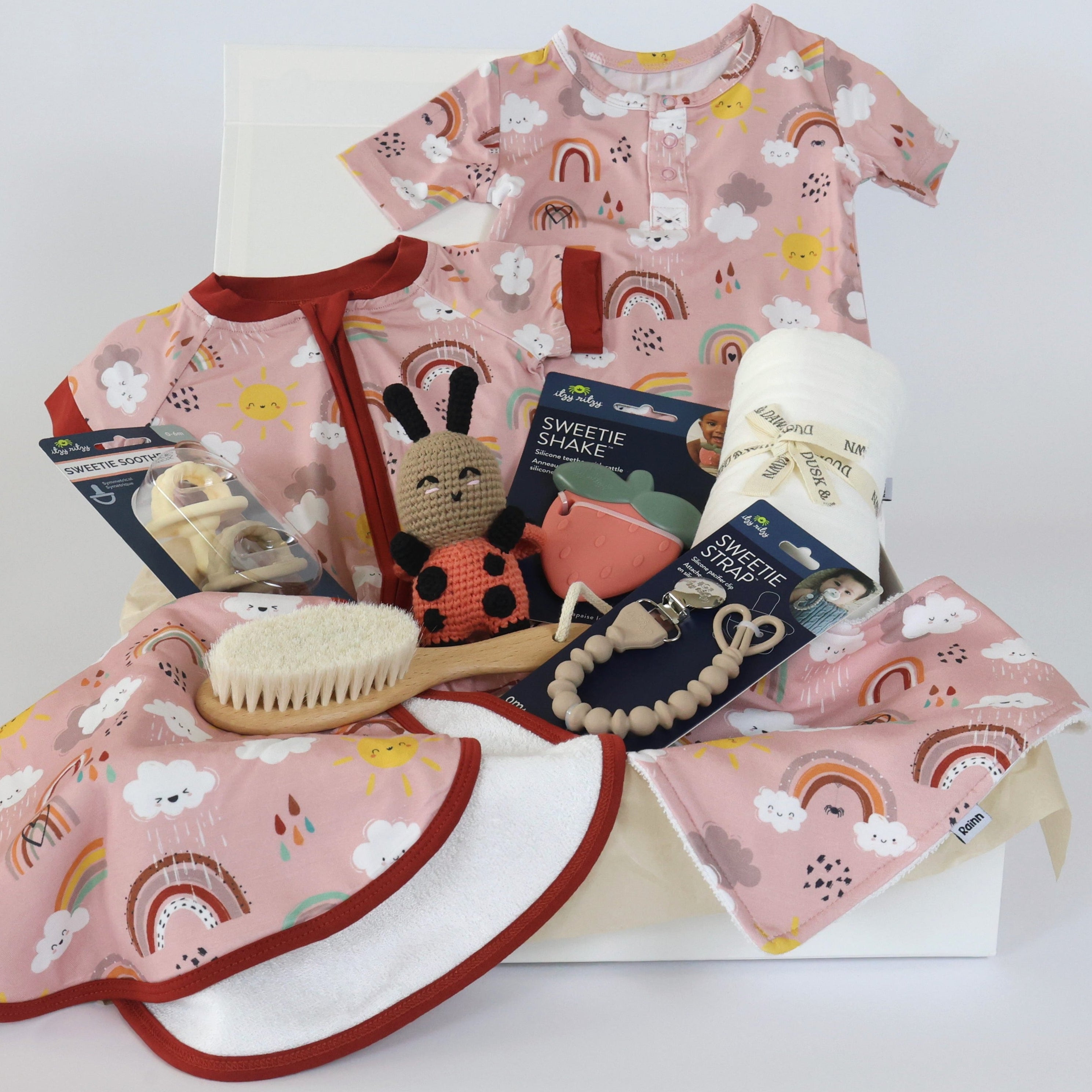 Newborn gift set for girls featuring clothing, toys, and accessories in soft pink with rainbow patterns.