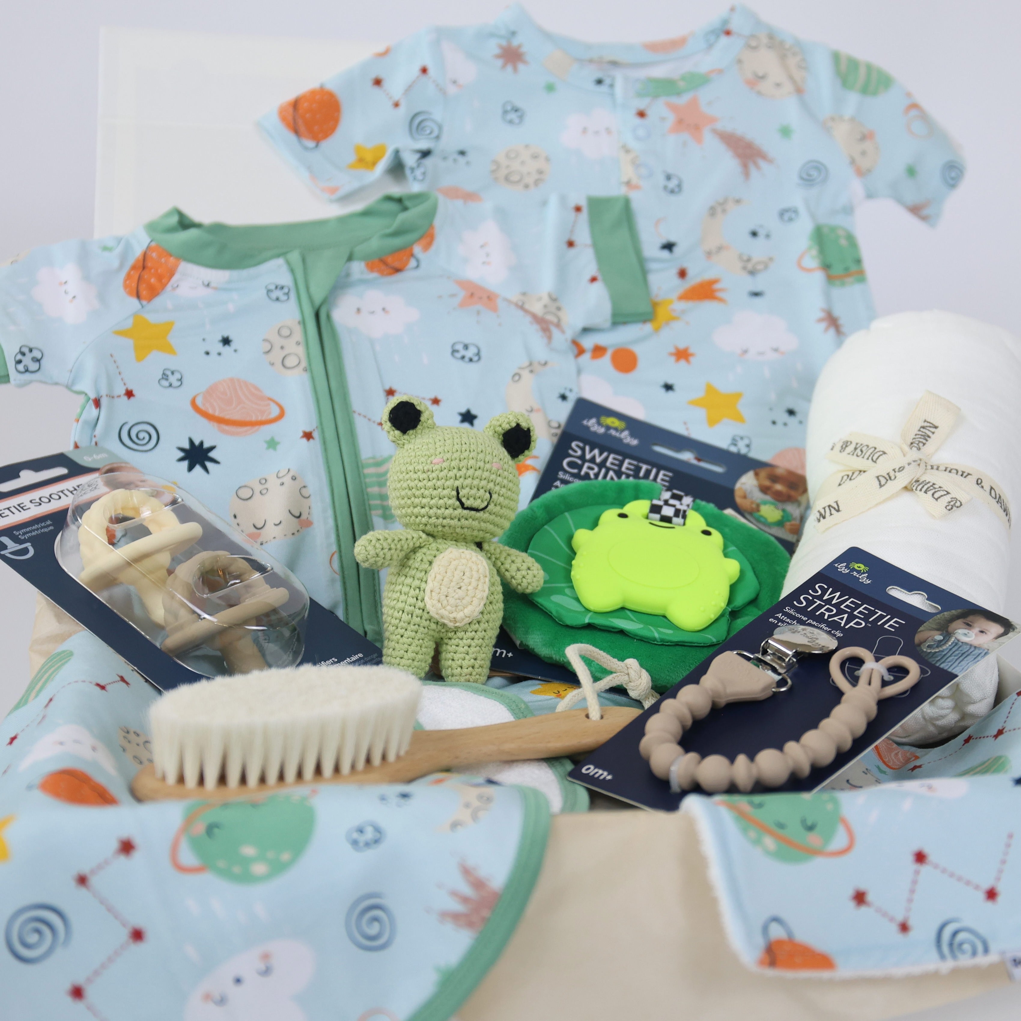 Newborn gift set for boys featuring playful outfits, toys, a brush, and accessories in a cozy arrangement.