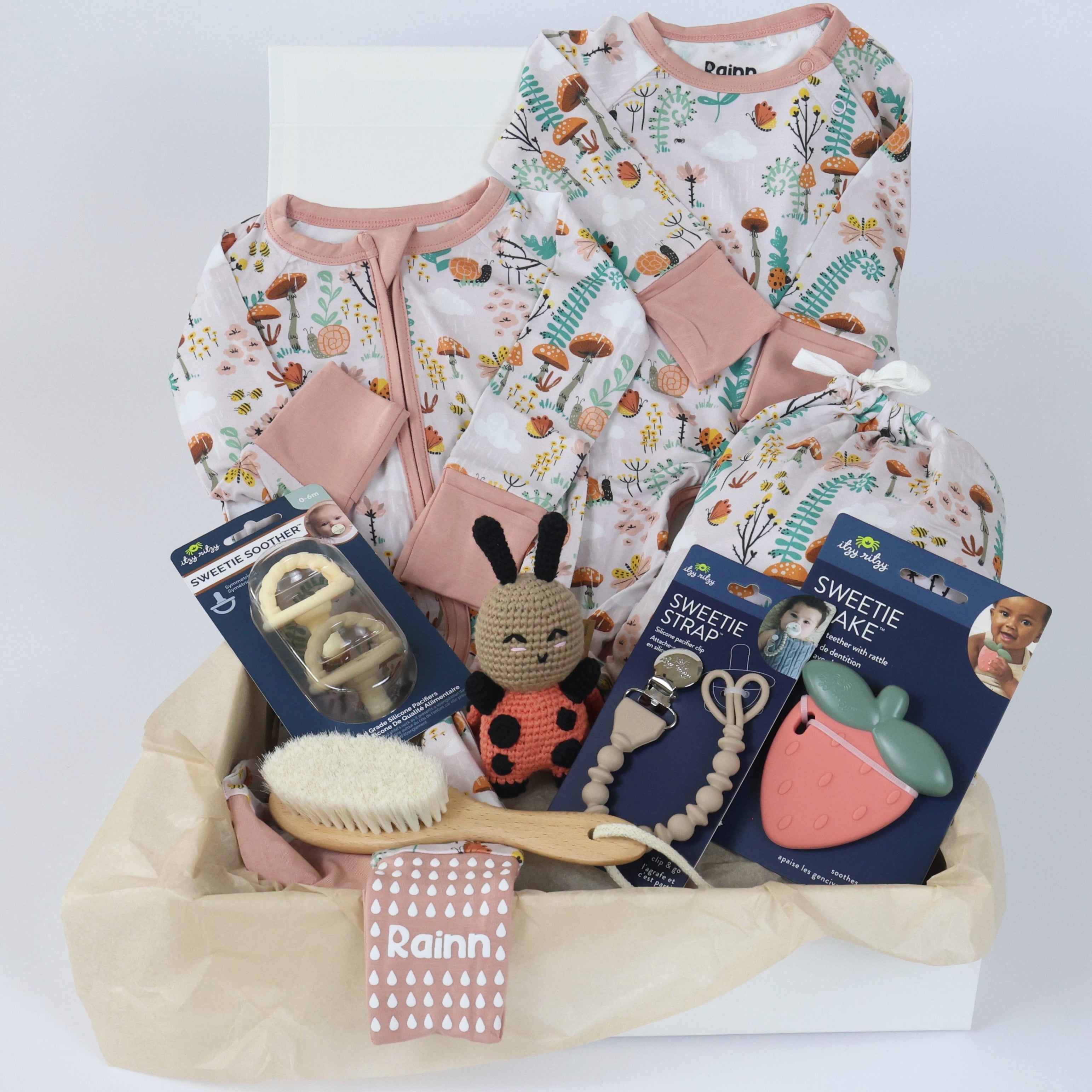 Newborn gift set for girls featuring cozy pajamas, pacifier, teether, and eco-friendly toys in decorative packaging.