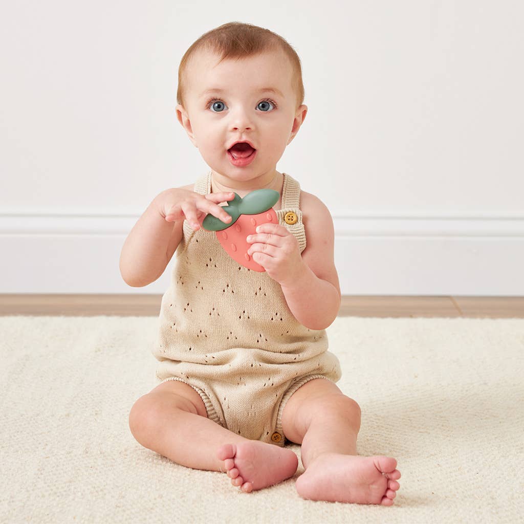 Excited baby sitting on a soft rug, holding a colorful silicone teething rattle. Perfect for teething relief!